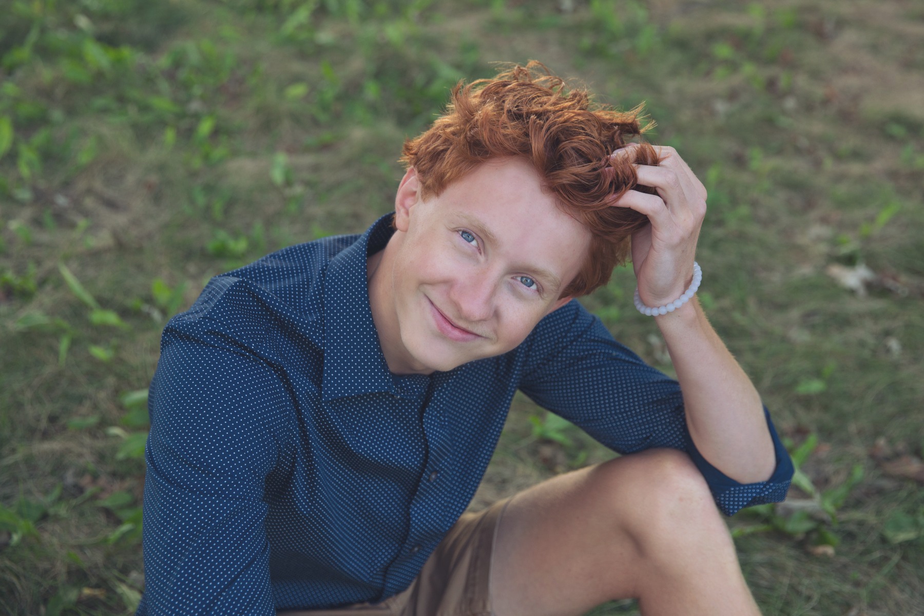 red headed senior boy sits in the grass