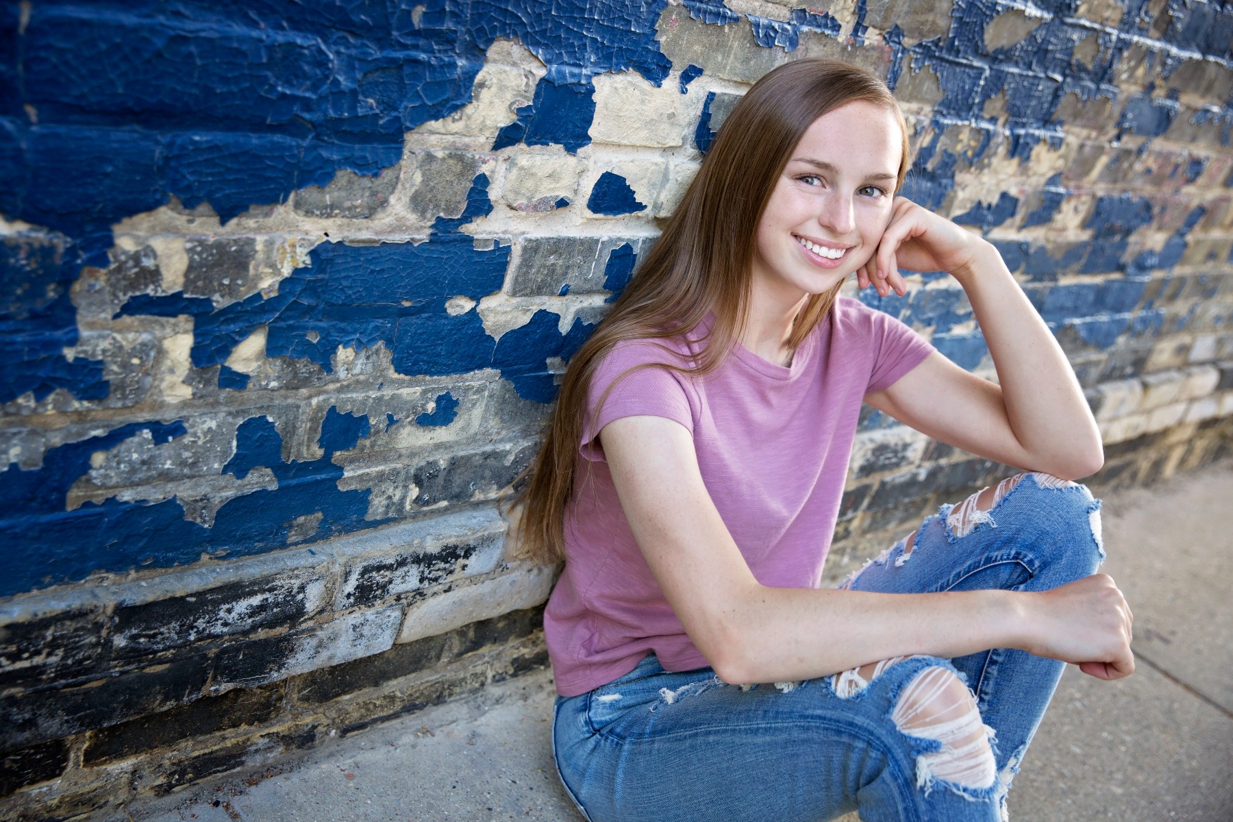 hs senior girl sits against a blue brick wall