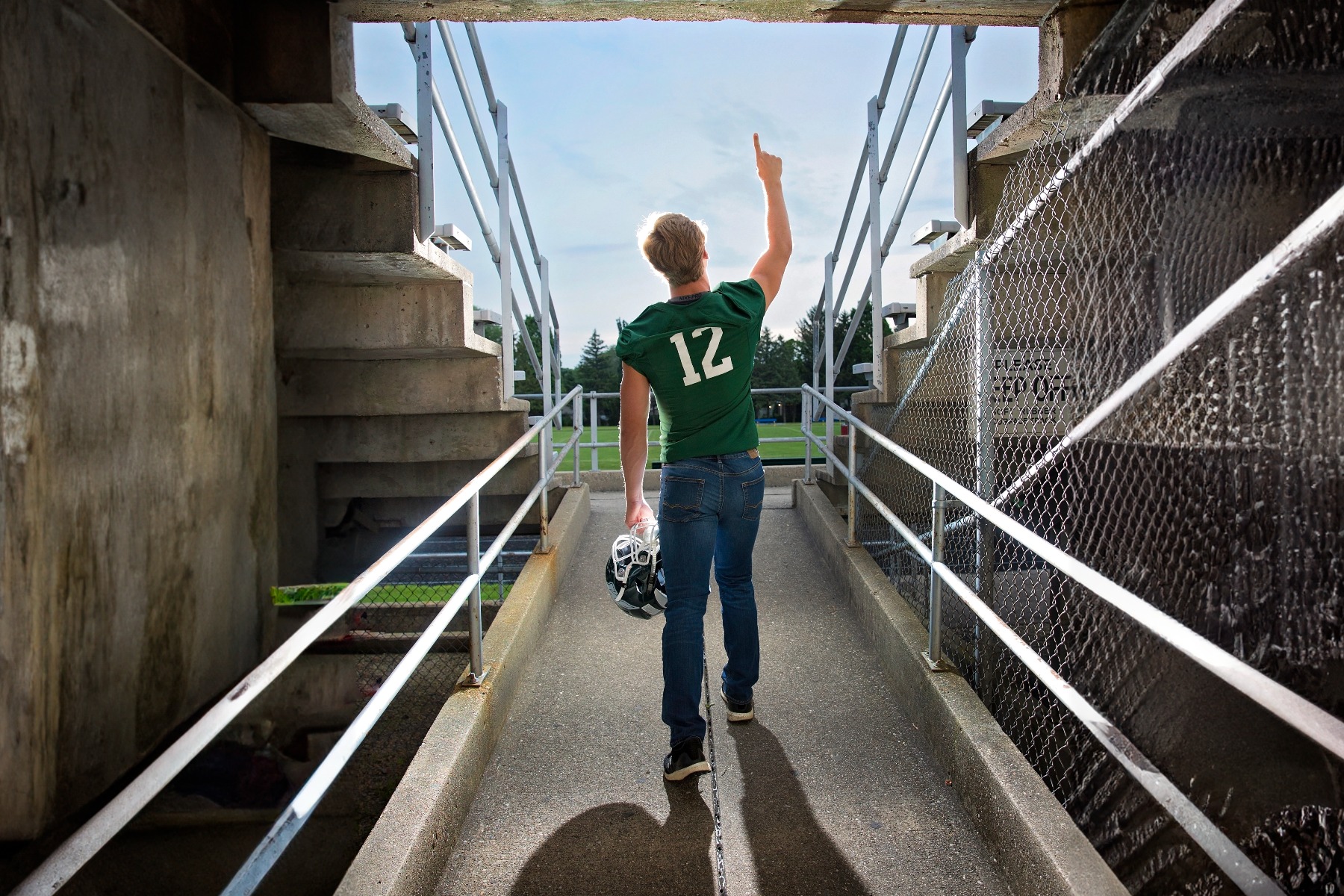 hs senior boy poses on a the entrance to the football field