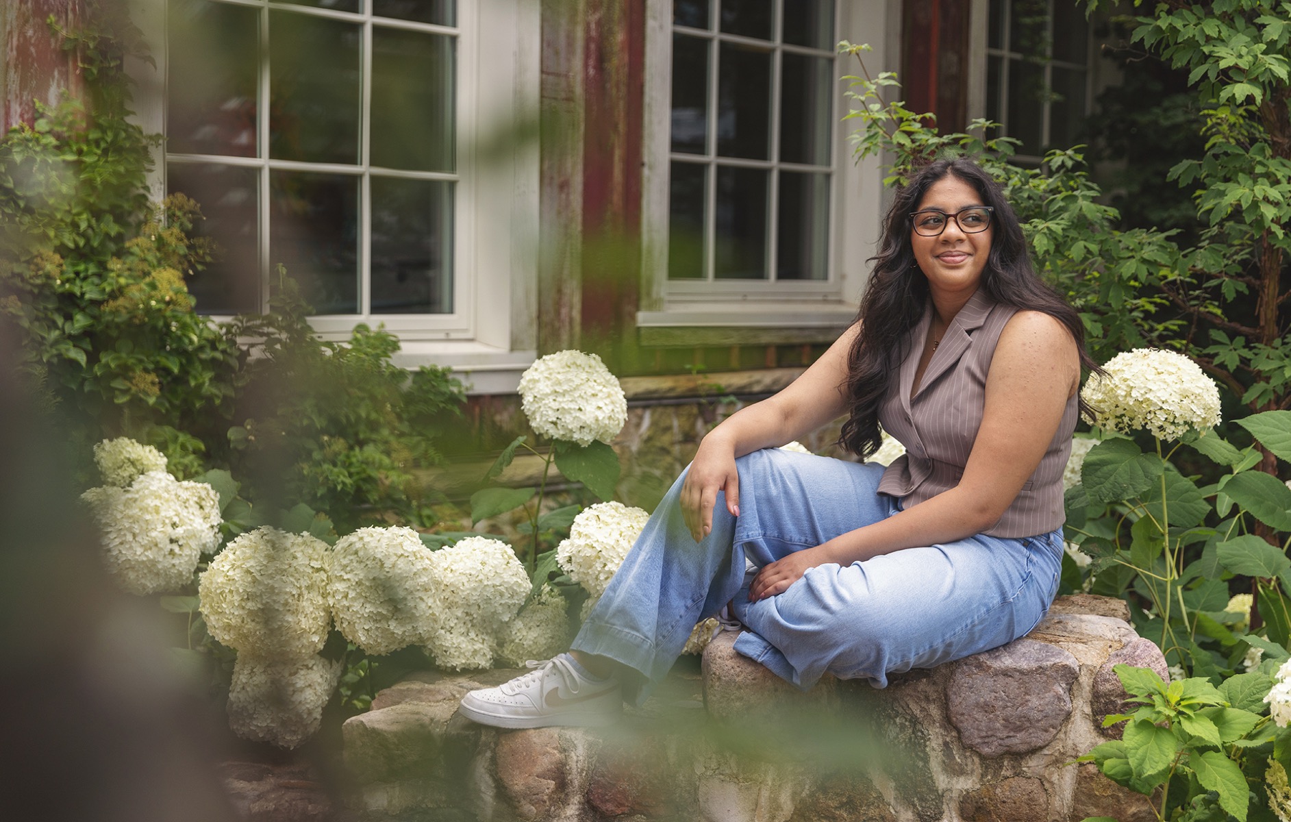 high school senior girl sits on a ledge amongst hydrangea blossoms