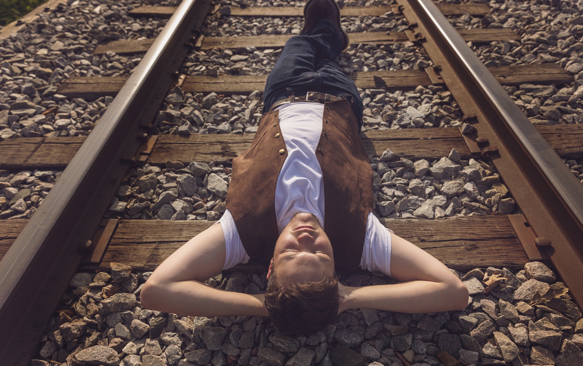 high school senior boy lays flat on his back on a row of train tracks