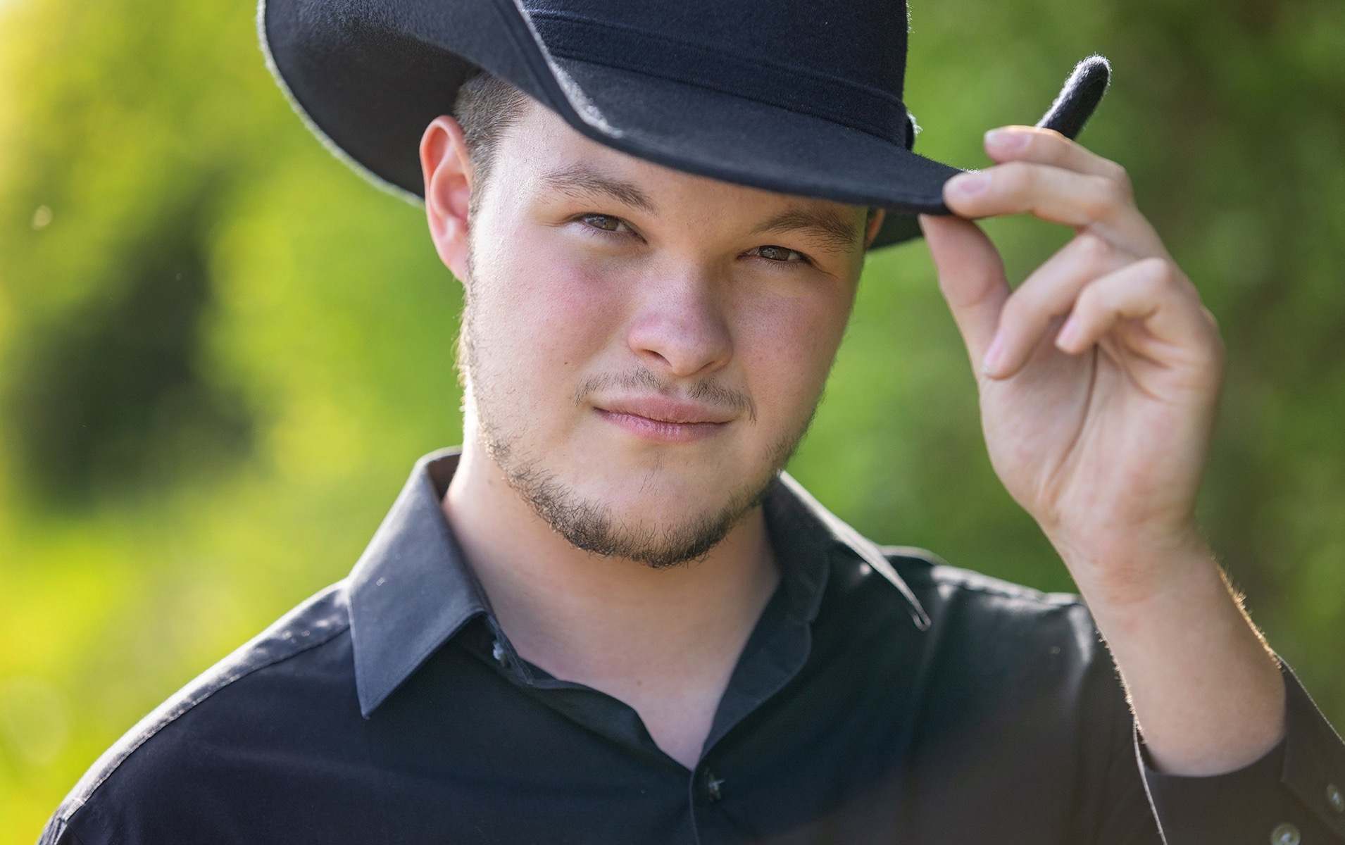 high school senior boy poses with a large black cowboy hat