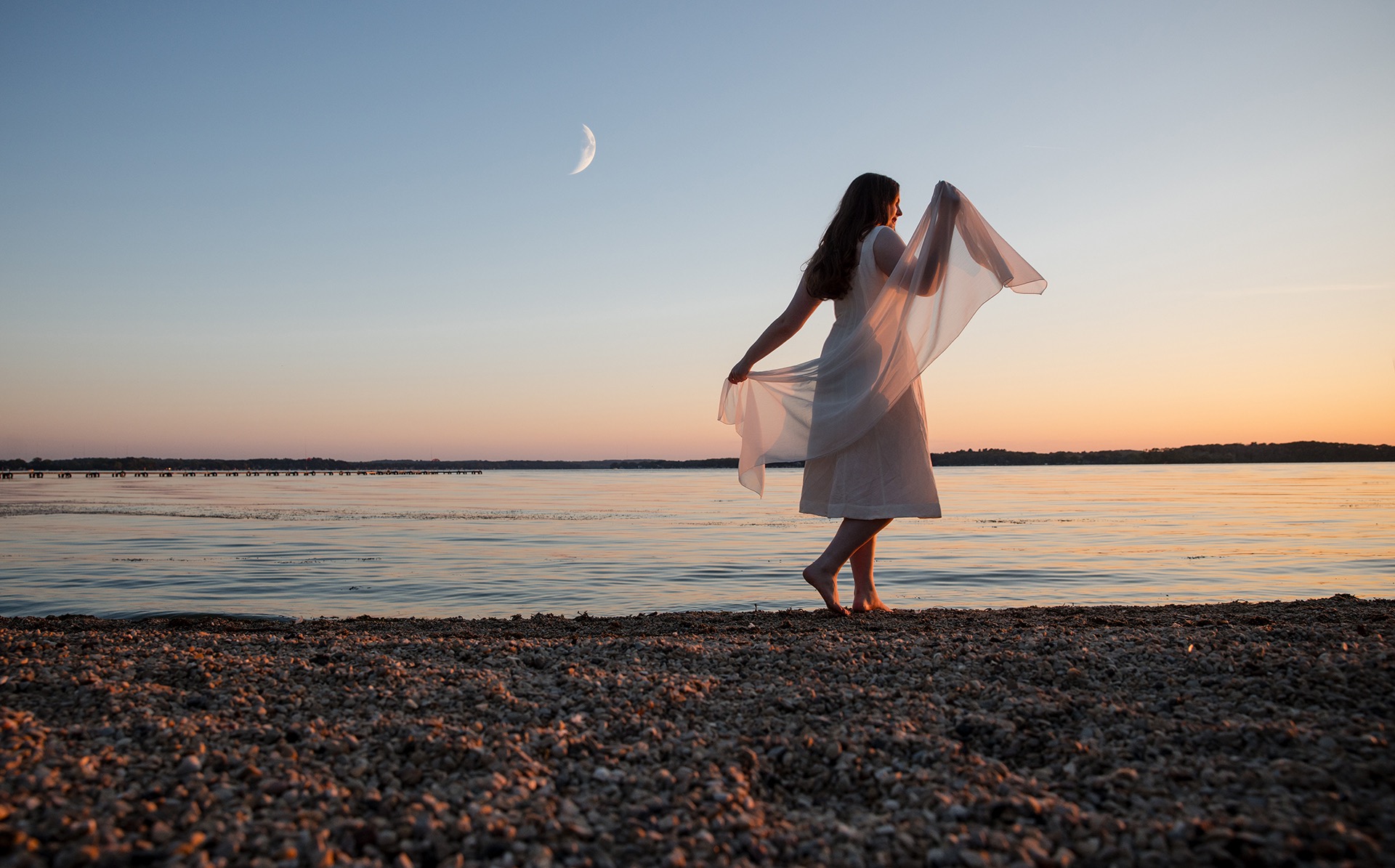high school senior girl dances in silhouette along the shoreline of a beach