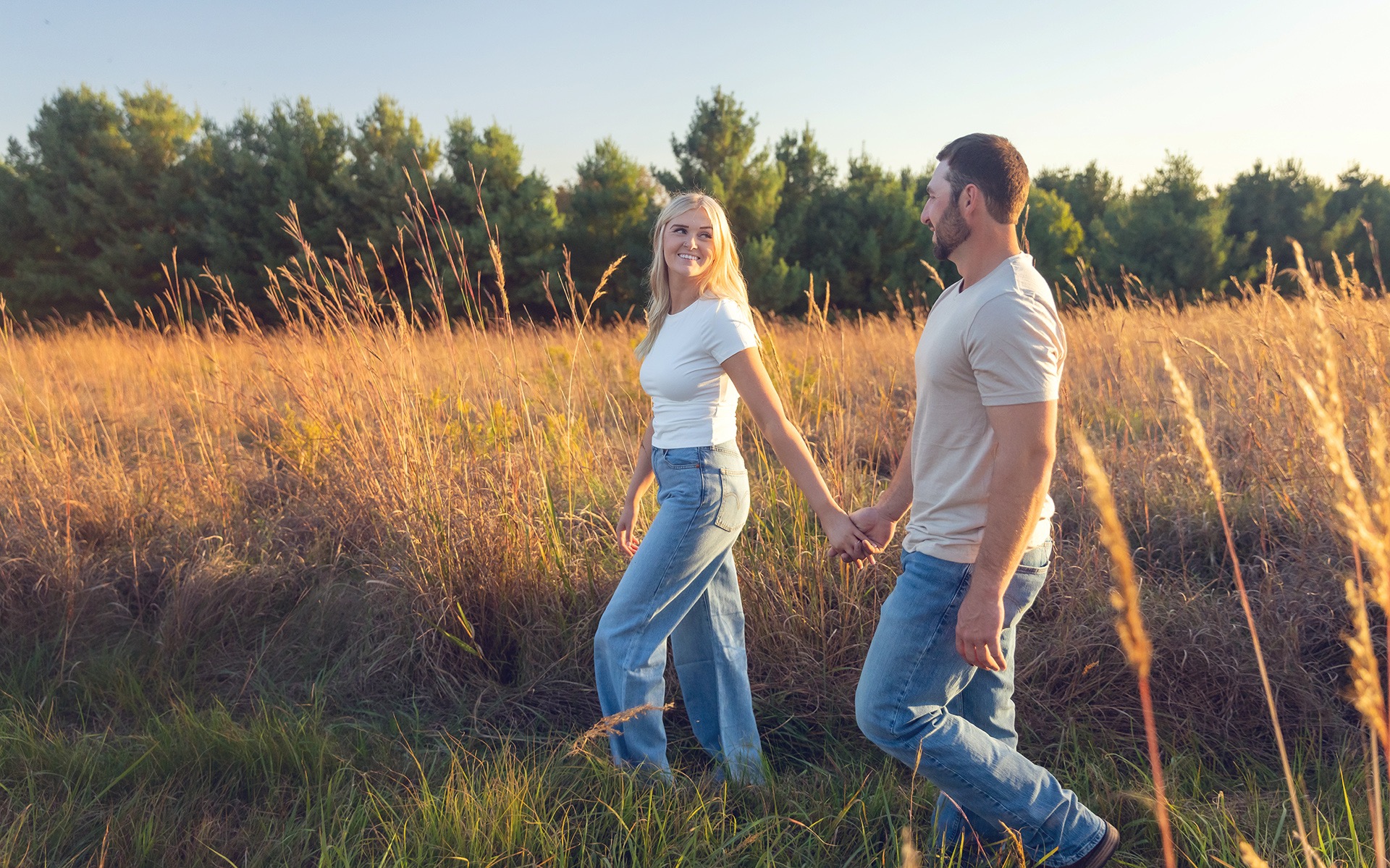 a young engaged couple walks down a path in a field of tall grasses